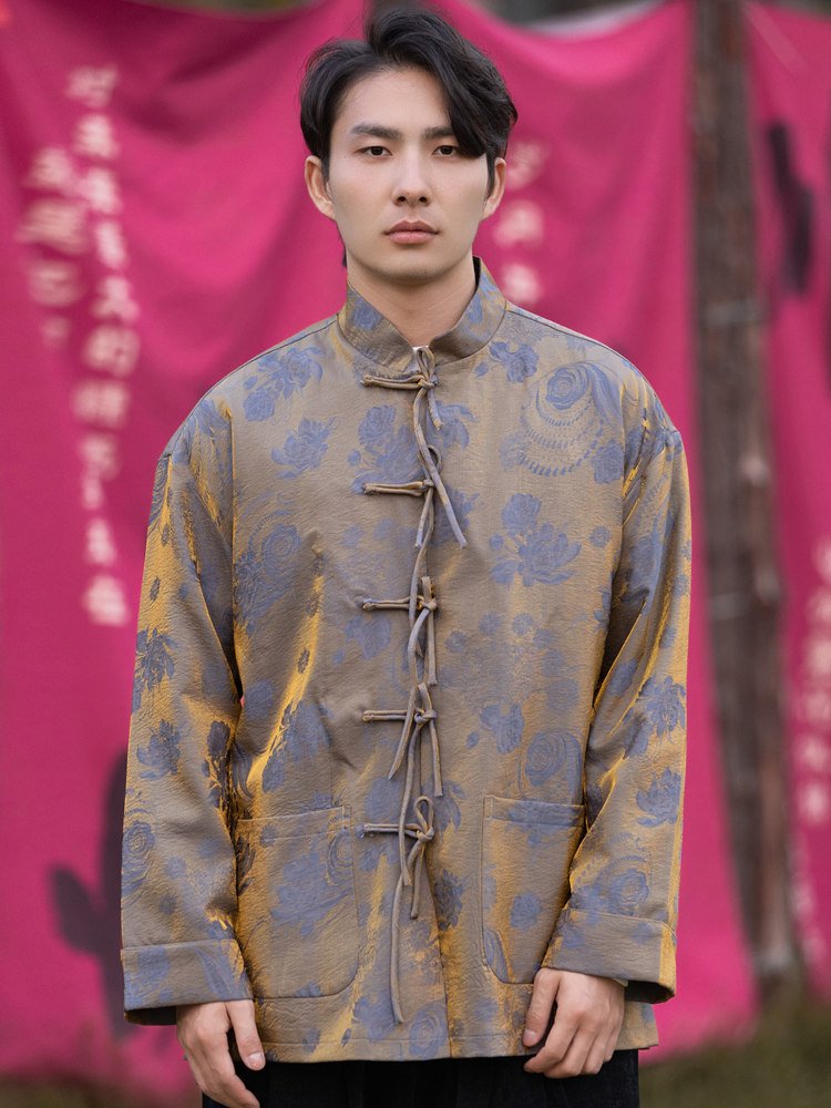 Close-up view of a man wearing a blue Tang-style Chinese brocade jacket with rich jacquard patterns and frog button closure.