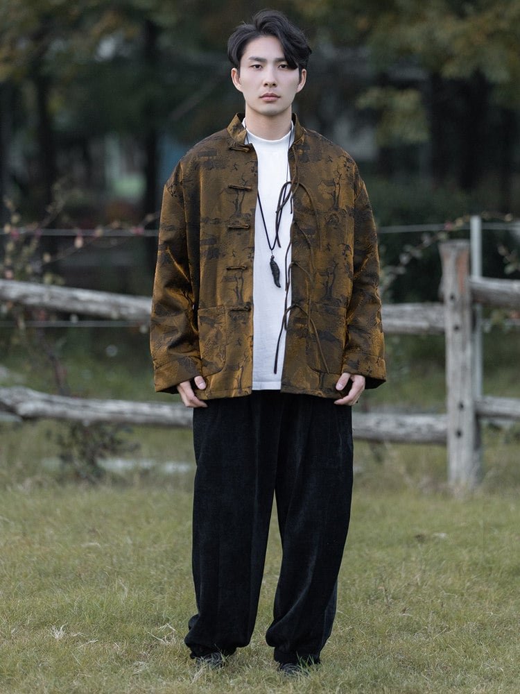 Full-body outdoor view of a man wearing a yellow Chinese brocade jacket with jacquard fabric and frog button design.