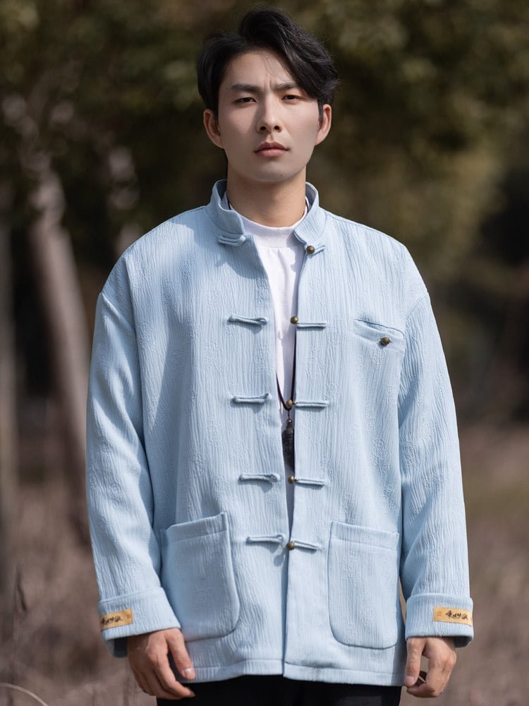 Close-up front image of a light blue Chinese Tang jacket showing the mandarin collar, frog buttons, and textured fabric.