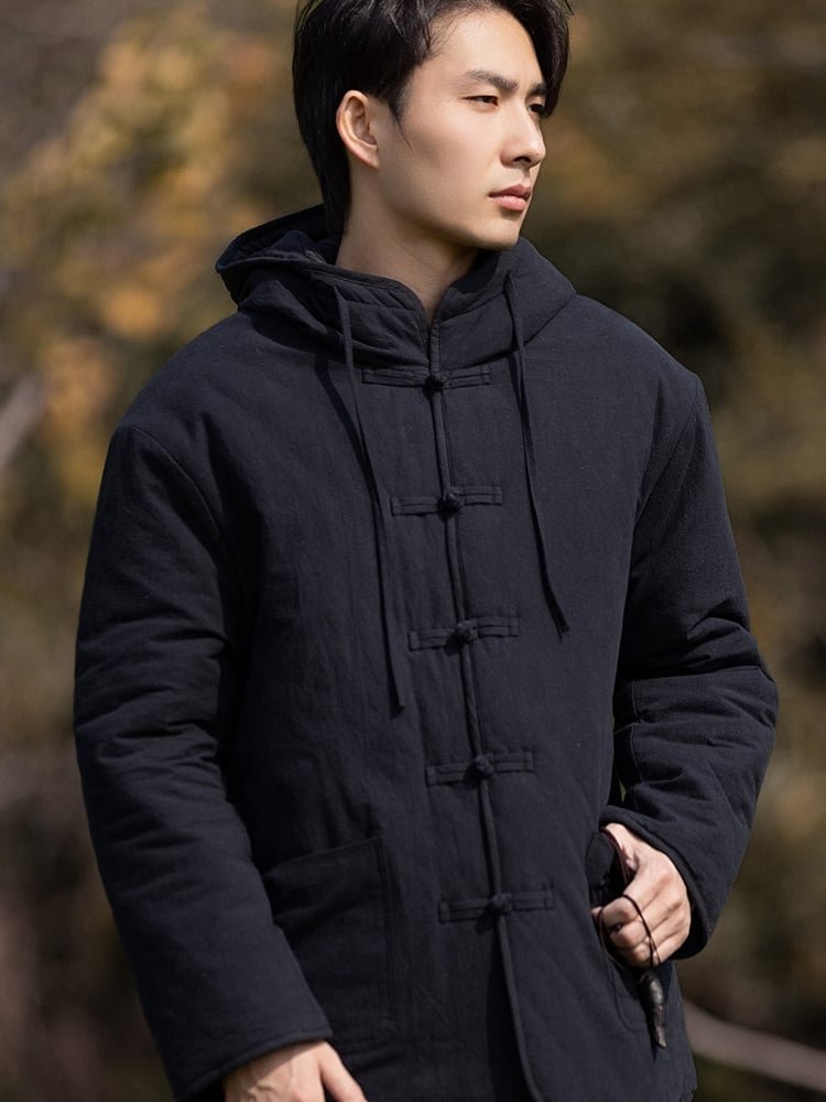 Side view of a man wearing a black hooded Chinese winter jacket with frog buttons and padded construction.