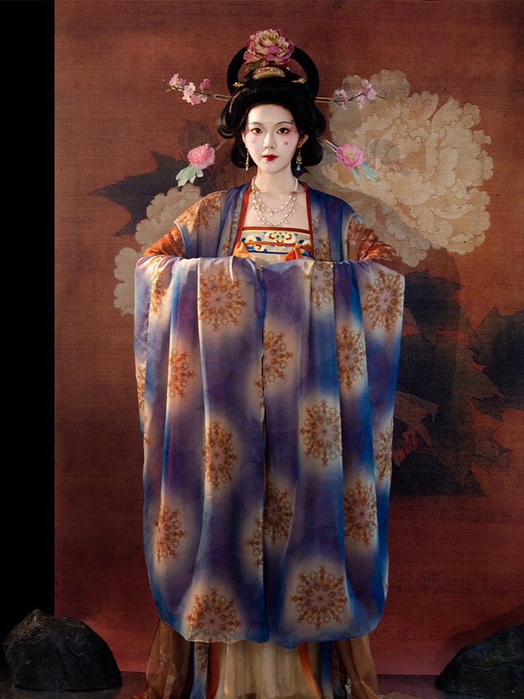 Model wearing Tang dynasty mural hanfu dress in blue, gold and orange gradient with wide sleeves in a full-body standing pose.
