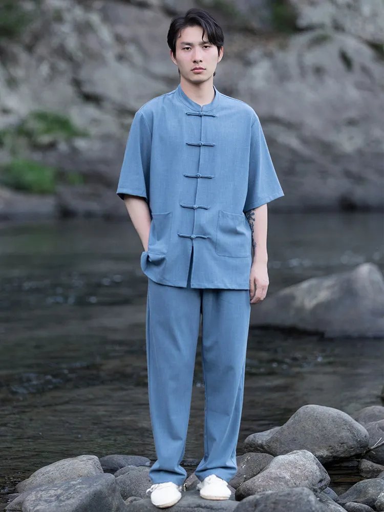 Model in a blue Chinese mandarin collar summer outfit with frog buttons, standing with hands in pockets by the river.