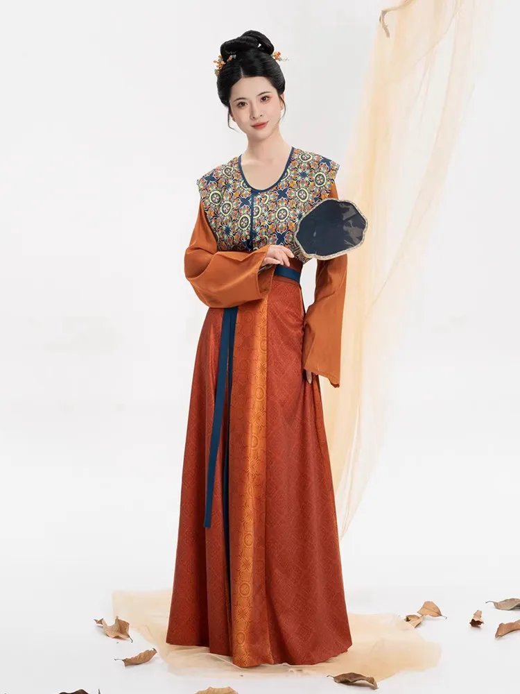 Model posing in Tang dynasty inspired Hanfu dress with vibrant orange skirt and blue-green printed vest.